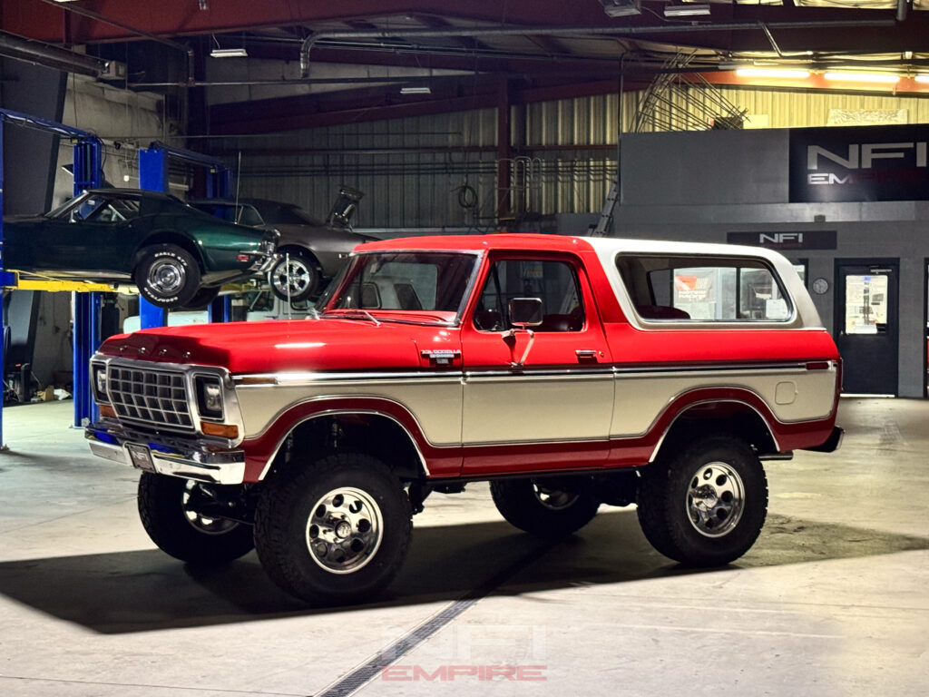 Side view of a red 1978 Ford Bronco featuring custom '7.3L Godzilla Bronco' and 'NFI Empire' badges, showcasing the vehicle's restomod transformation.