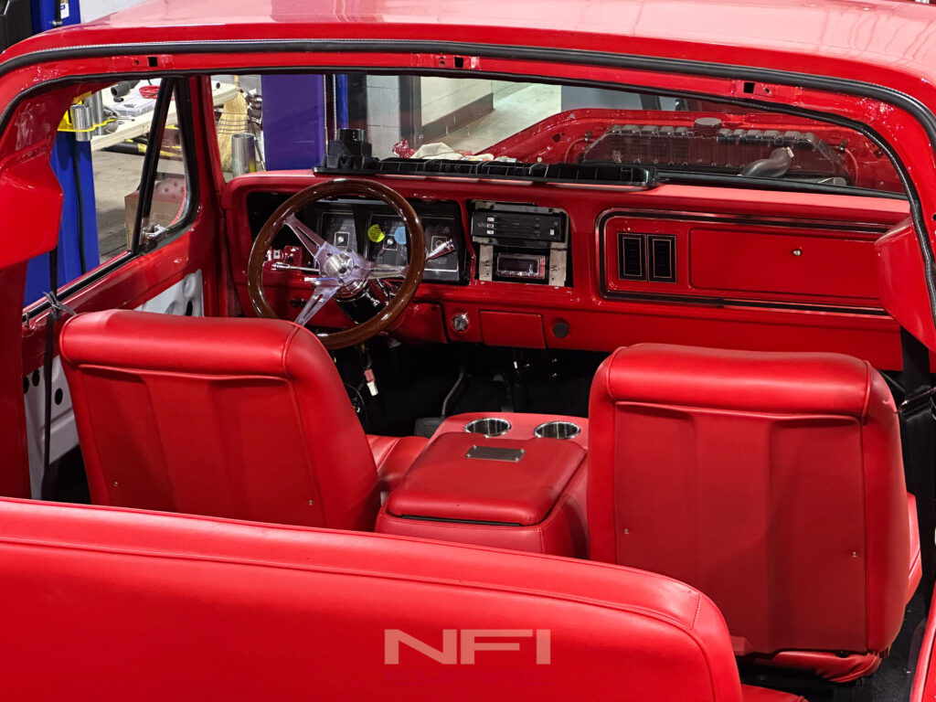 Interior view of a red vintage Ford Bronco featuring hand-stiched red leather seats, a wooden steering wheel, and a vibrant dashboard during a restomod project by NFI Empire.
