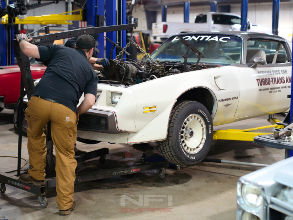 engine being pulled out of a white Pontiac Trans Am in NFI Empire's service garage